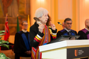 An Elder holding an eagle feather speaks at the podium during the convocation ceremony.
