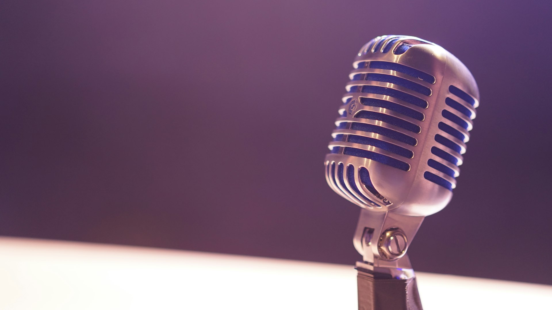 A professional studio condenser microphone in soft light against a dark background, evoking broadcast, podcasting and public discourse.