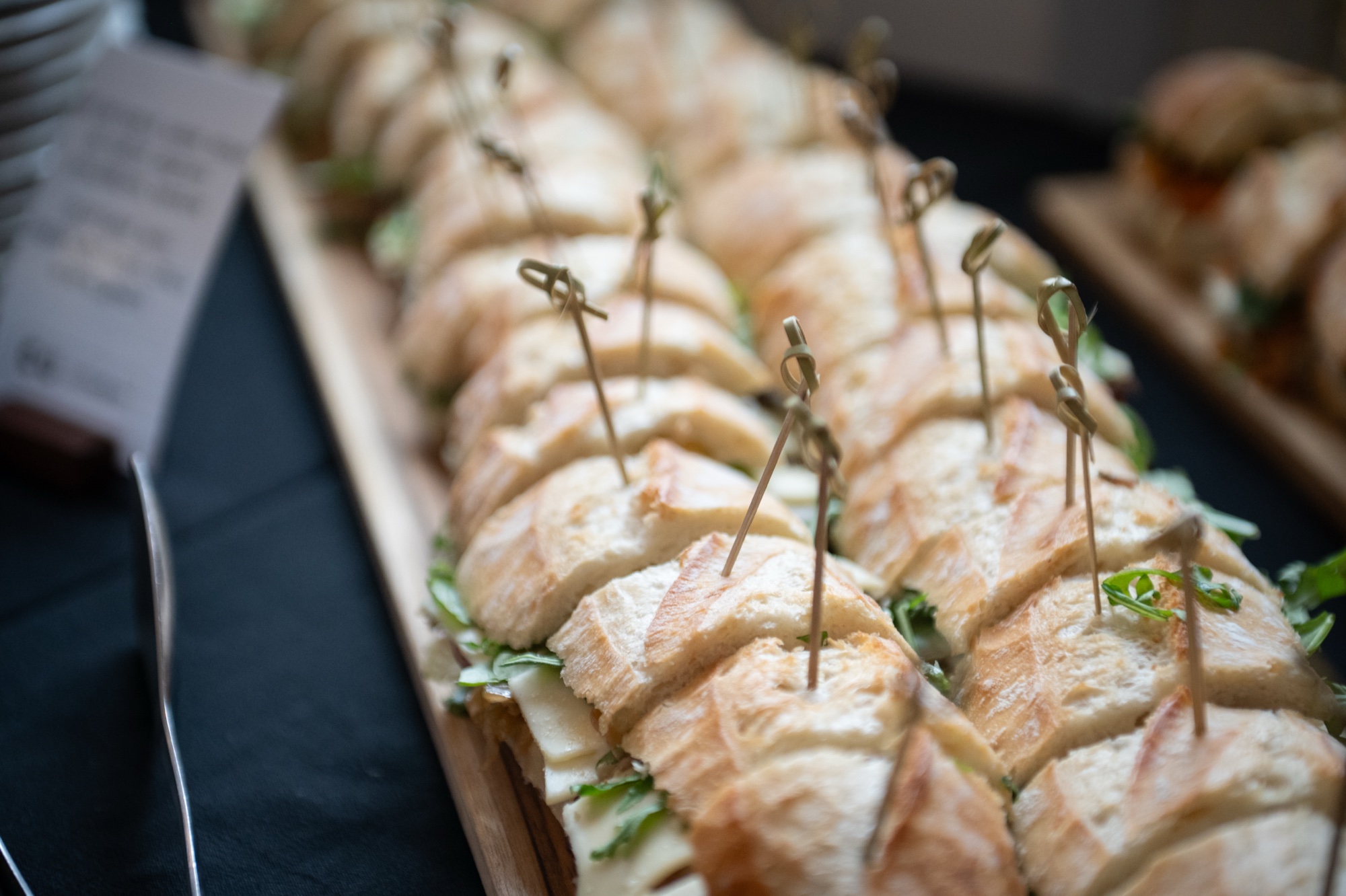 Rows of cocktail sandwiches with skewers on a wooden board