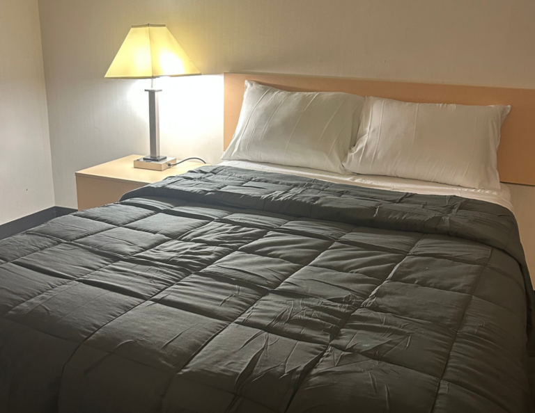 Residence bedroom with a double bed, dark grey duvet, white pillows and a bedside lamp